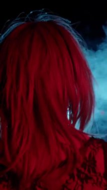 Dar elbiseli travesti dışarıda dikiliyor ve kırmızı ışıkta vapur kullanıyor. Orta çekim