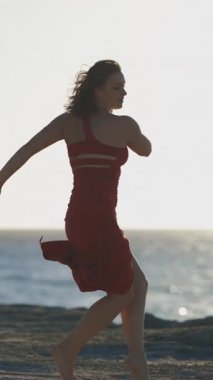 Gün batımında kayalık bir sahilde etkileyici hareketler sergileyen zarif dansçı.