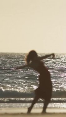 Esnek bir kadın dans ediyor ve gün batımında deniz kıyısında köprüde duruyor. Orta çekim