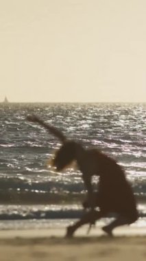 Genç kadın batımında sahilde dans