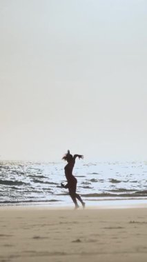 Gün batımında plajda tek başına dans eden kırmızı elbiseli zarif genç bayan. Orta çekim