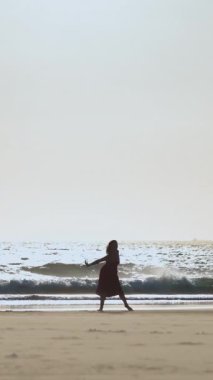 Genç kadın batımında sahilde dans