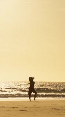 Gün batımında sahilde dans eden bir kadının silueti.