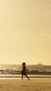 Sisli günbatımında kumsalda tek başına dans eden uzun elbiseli zarif genç bir kadın. Orta çekim