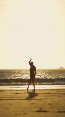 Gün batımında plajda yürüyen kırmızı elbiseli zarif bir kadın. Orta çekim