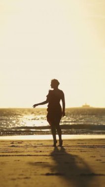 Gün batımında sahilde yürüyen bir kadının silüeti.