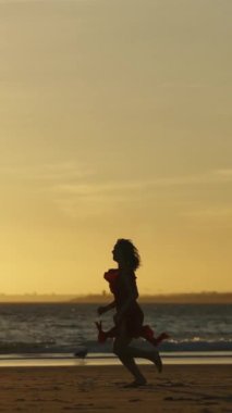 Genç kadın gün batımında sahilde dans edip koşuyor.
