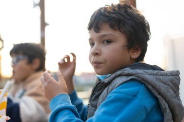 Dışarıda abur cubur yiyen genç çocuk meraklı bakışlarla izleyiciyi cezbediyor.