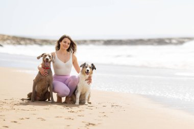 İki sevgili köpeğiyle kumsalda güneşli bir günün tadını çıkaran bir kadın.