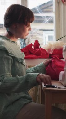 Bir kadın dikiş makinesine kırmızı bir elbise diker ve çerçeveyi terk eder. Orta çekim