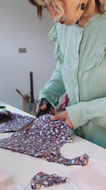 Bir kadın tasarımcı, makas kullanarak çiçek kumaşından desenler kesiyor. Orta çekim