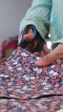 Bir kadın makas kullanarak çiçekli kumaştan desenleri dikkatlice keser. Orta çekim