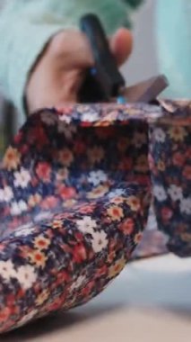 Bir kadın çiçek kumaşındaki desenleri makas kullanarak kesiyor. Orta çekim