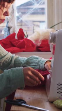 Kadın tasarımcı dikiş makinesine kırmızı kumaş dikiyor. Orta çekim