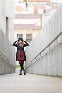 Modern beton bir yolda kırmızı ekose etekli ve şapkalı şık bir kadın.