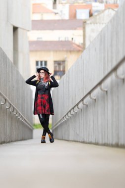 Beton bir alt geçitte duran genç bir kadın kameraya bakıyor ve gözlüklerini ayarlıyor.