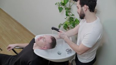 Profesyonel bir kuaförde saçını yıkatan ve yıkayan bir erkek müşteri.