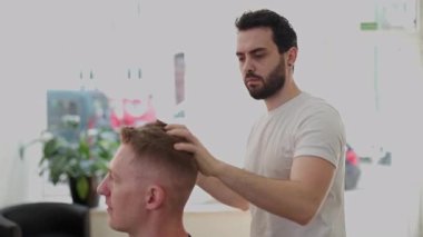 Erkek kuaför modern bir güzellik salonunda bir adamın saçını balmumuyla şekillendirmek için ellerini kullanıyor.