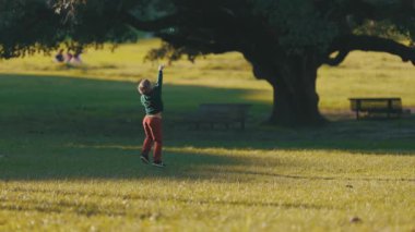 Parkta neşeyle oynayan genç bir çocuk güneşli bir öğleden sonra sabun köpüğü yakalamak için zıplıyor.