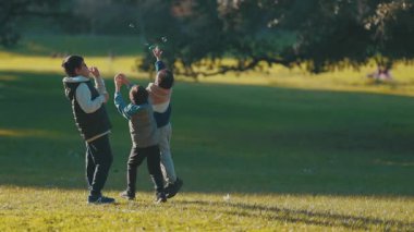 Güneşli bir günde güneşli bir parkta sabun köpüğü kovalayan ve oynayan üç mutlu çocuk.