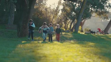 Neşeli çeşitli çocuklar, güneşli bir parkta yeşil çimlerde oynayıp koşuyorlar.