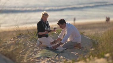 Kumsalda romantik bir piknik sırasında kırmızı şarapla kadeh kaldıran sevecen erkek ve kadın.