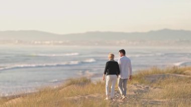 Güzel okyanus dalgalarına doğru kumlu bir yolda yürürken el ele tutuşan sakin bir çift.