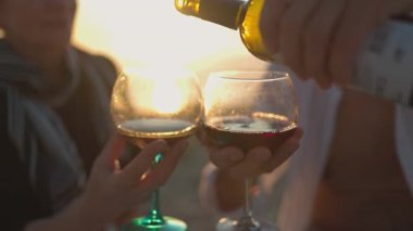 Olgun bir çift kumsalda romantik bir piknik yapıyor ve altın bir günbatımına karşı şarap içiyor.