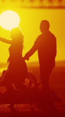 Rıhtımda romantik bir dans başlıyor. Güneş altın bir renk alıyor ve arka planda bir köprü var..