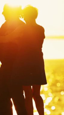 Deniz köprüsünün yanında dans eden yaşlı bir çiftin silueti. Arka planda büyük bir yolcu gemisi, gün doğumu.