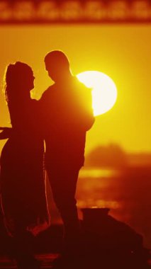 Siluet - bir çift arasında samimi bir kucaklaşma yakalar, gün batımının yumuşak renkleri ve arkaplanda köprü.