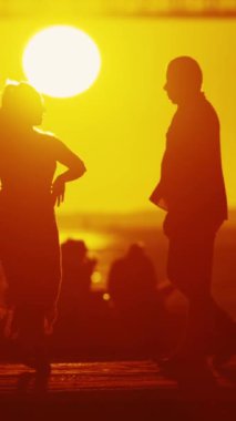 Bir çift silueti, arkasında bir köprünün mimari harikası ile parlak bir günbatımına karşı duruyor..