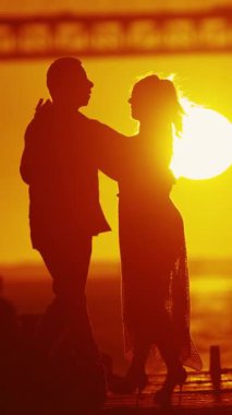 Yaşlı bir çift - dansçı silueti güneş tarafından aydınlatılır, günbatımı ve köprünün zemininde dans etmenin zarafetini sergilerler..