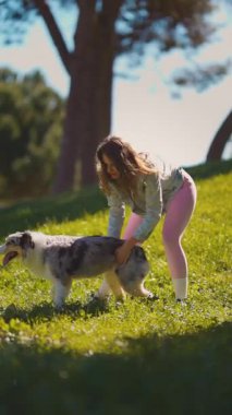 Sevecen genç bir kadın, mutlu mavi merle Avustralyalı çoban köpeğini parkta okşuyor.