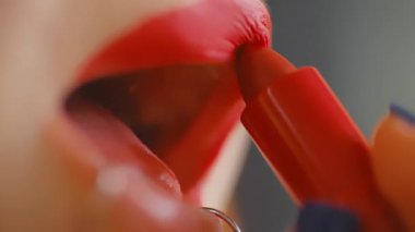 Dudaklarına canlı kırmızı ruj sürerken bir kadının ağzının aşırı yakın çekimi.