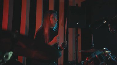 Uzun saçlı genç bir kadın renkli ışıklarla enerjik bir müzik stüdyosunda davul çalıyor.
