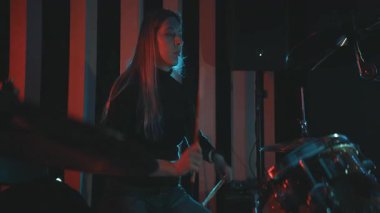 Genç bir kadın, performans sırasında kırmızı ve mavi ışıklarla karanlık bir sahnede enerjik bir şekilde davul çalıyor.