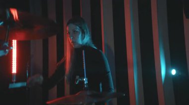 Kırmızı ve mavi ışıklı bir müzik performansı sırasında davul çalan tutkulu kadın müzisyen.