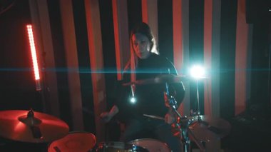 Yetenekli bayan müzisyen yaratıcı ışıklandırması olan bir müzik stüdyosundaki bateri setinde enerjik bir şekilde ritim çalıyor.
