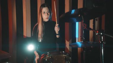 Karanlık bir stüdyoda grup provası sırasında tutkulu bir şekilde davul çalan enerjik kadın müzisyen.