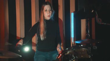 Genç bir kadın prova sırasında müzik stüdyosunda davul çalıyor.