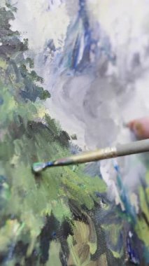 Kadınlar, bir çalı ve yağlı boya kullanarak ağaçlarla çevrili bir dağ manzarasının resmini yapıyorlar.