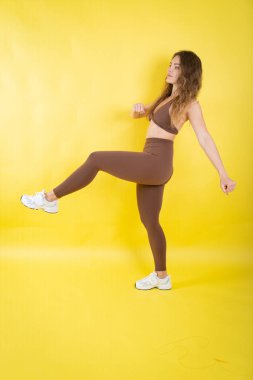 Açık sarı arka planda spor yapan aktif bir kadın.