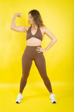 Kol kaslarını esneten bir kadın kahverengi spor giyimde güç ve zindelik gösteriyor.