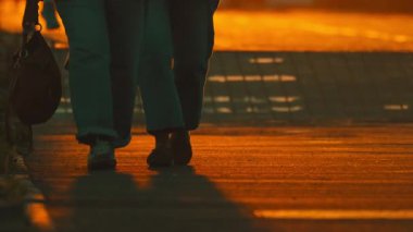 Güzel bir günbatımında şehir kaldırımında yürüyen romantik bir çiftin alt vücut görüntüsü.