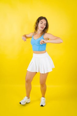 Genç bir kadın enerjik hareket ediyor, parlak sarı bir arka planda aktif spor kıyafeti giyiyor.