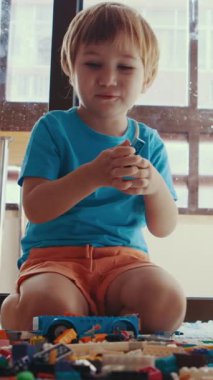 Oyuncaklarla çevrili yerde oturan küçük bir çocuk.