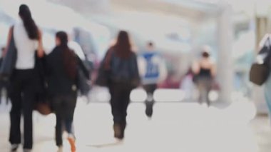 Bir grup anonim insanın güneş ışığıyla aydınlanmış kamusal alanda yürüyüp gitmelerinin odak noktası dışında.