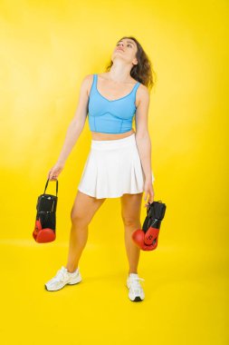 Sarı arka planda boks eldivenleri tutan kadın kararlılığını ve gücünü ifade ediyor.