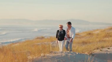 Güzel bir gün batımında kumlu bir sahilde el ele tutuşan ve birlikte yürüyen mutlu yaşlı çift.